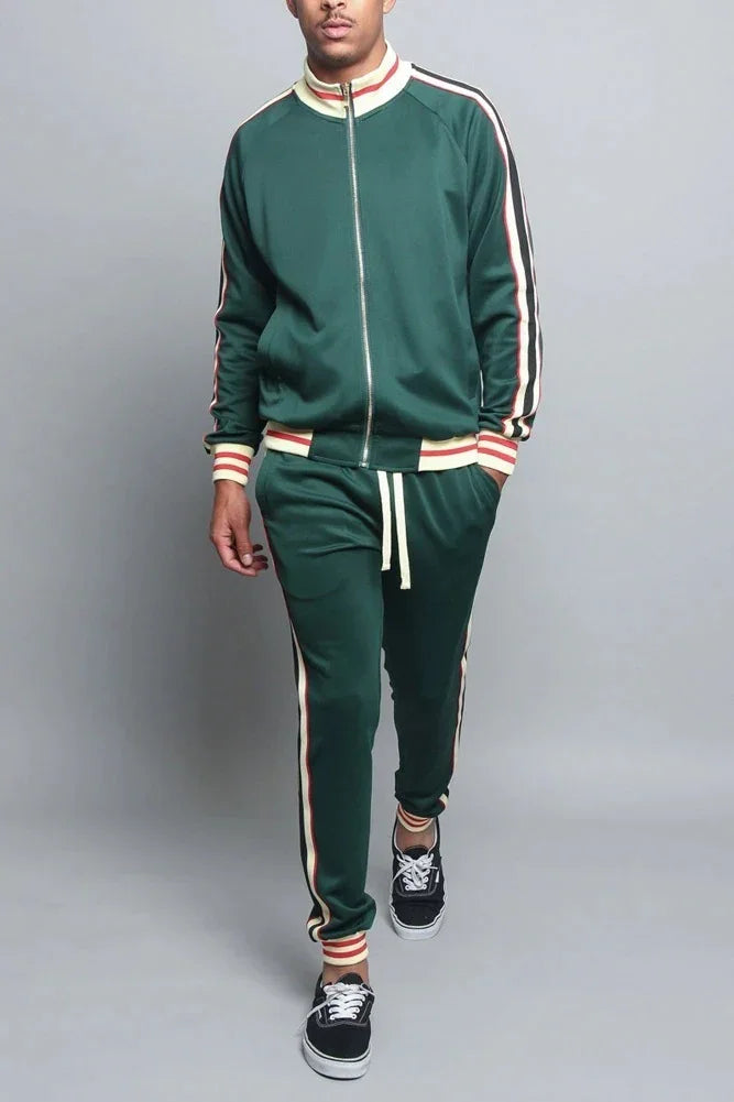 Man wearing green track suit with red and white stripes, black sneakers, neutral background
