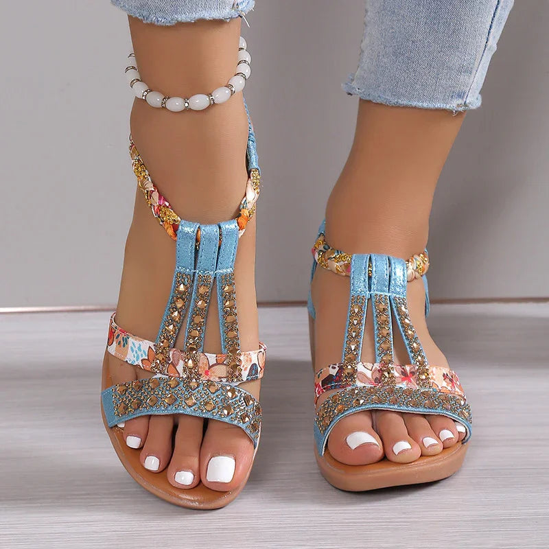 Women's blue and floral beaded sandals with white nail polish and ankle bracelet on wooden floor