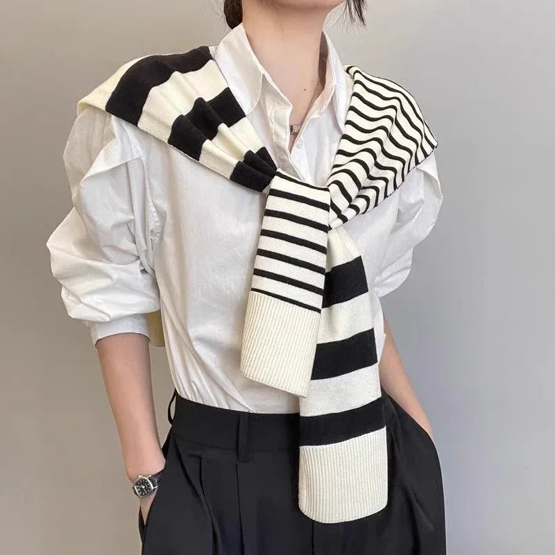 Person wearing white button shirt and black pants with a black and white striped sweater draped over shoulders