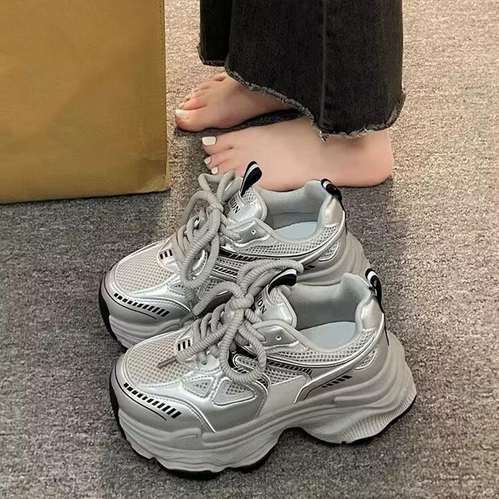 chunky silver platform sneakers with thick laces on gray carpet next to bare feet in black jeans