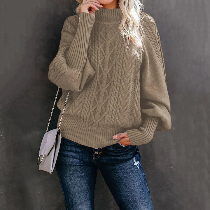 Woman wearing taupe cable knit sweater with balloon sleeves and distressed blue jeans, carrying gray purse
