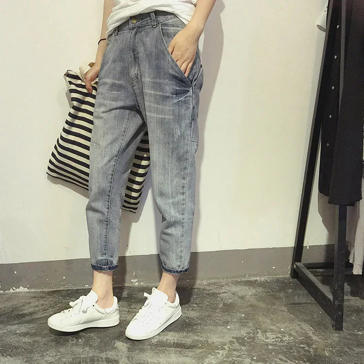Person wearing light washed denim jeans and white sneakers holding striped pillow indoors