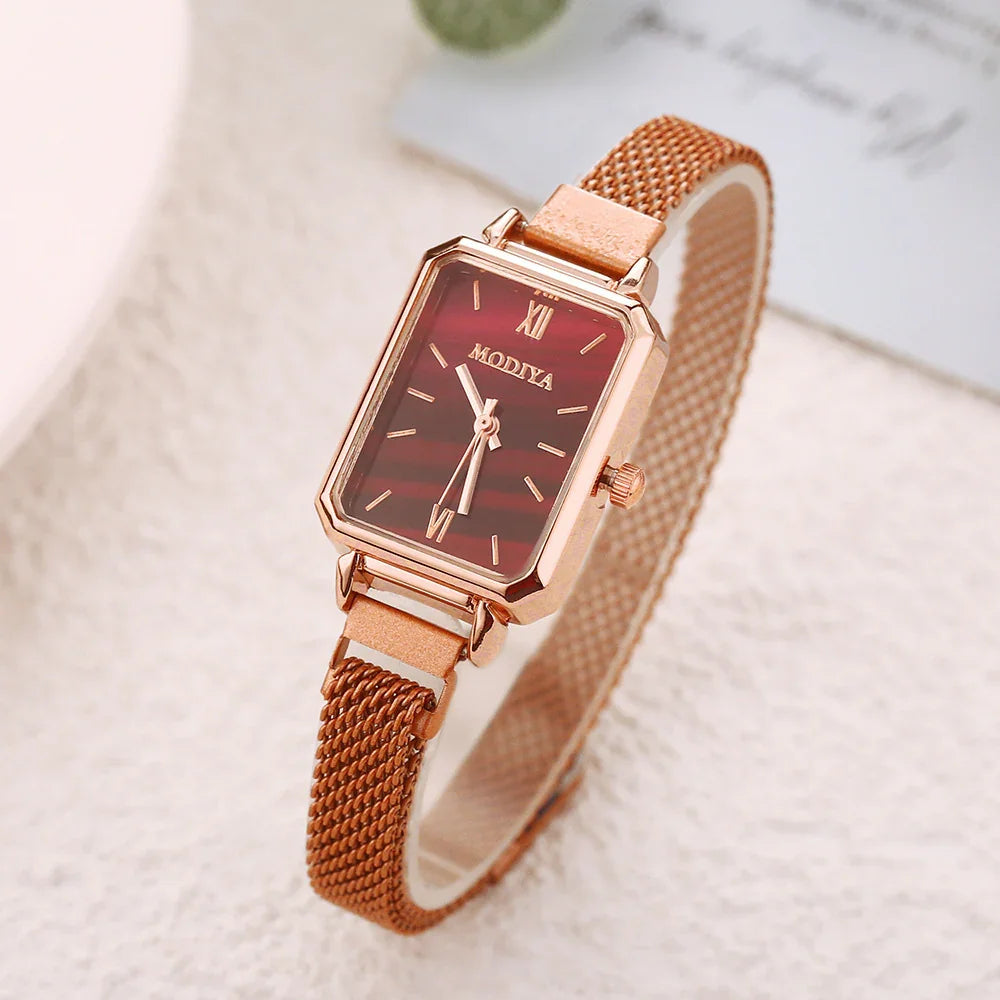 Rose gold wristwatch with rectangular red dial and mesh strap on light textured surface
