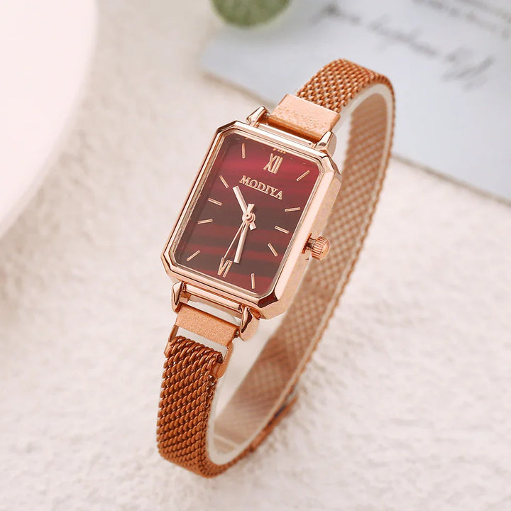 Rose gold wristwatch with rectangular red dial and mesh strap on light textured surface