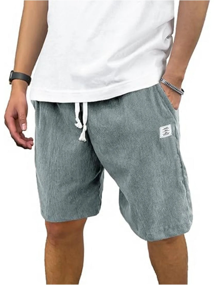 Man wearing gray striped drawstring shorts and a white t-shirt with wristwatch and bracelet