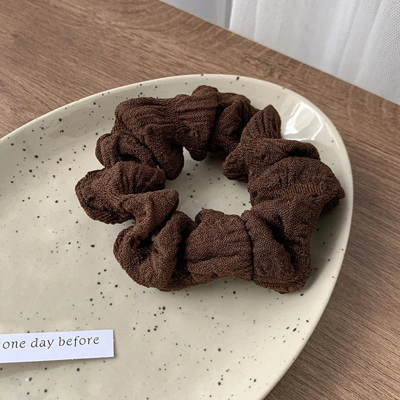 Brown textured fabric scrunchie on a speckled beige ceramic plate on a wooden table