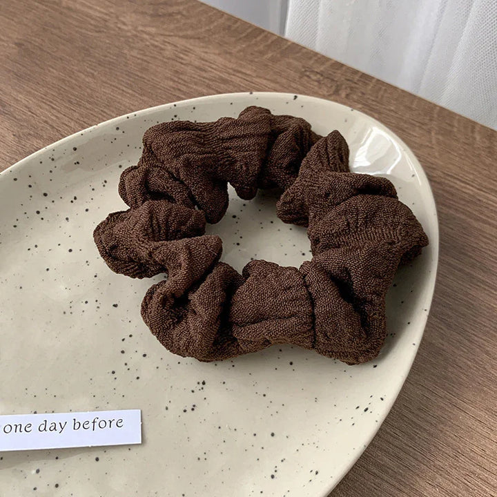 Brown textured fabric scrunchie on a speckled beige ceramic plate on a wooden table