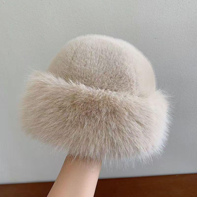 Hand holding a soft light beige faux fur bucket hat against a plain gray background