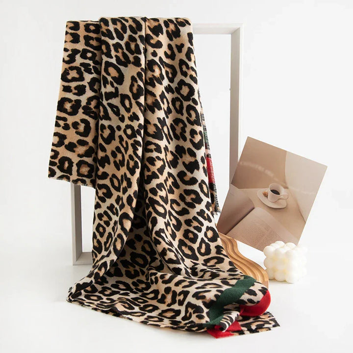 Leopard print scarf draped over white frame next to photo of coffee and book on wooden surface
