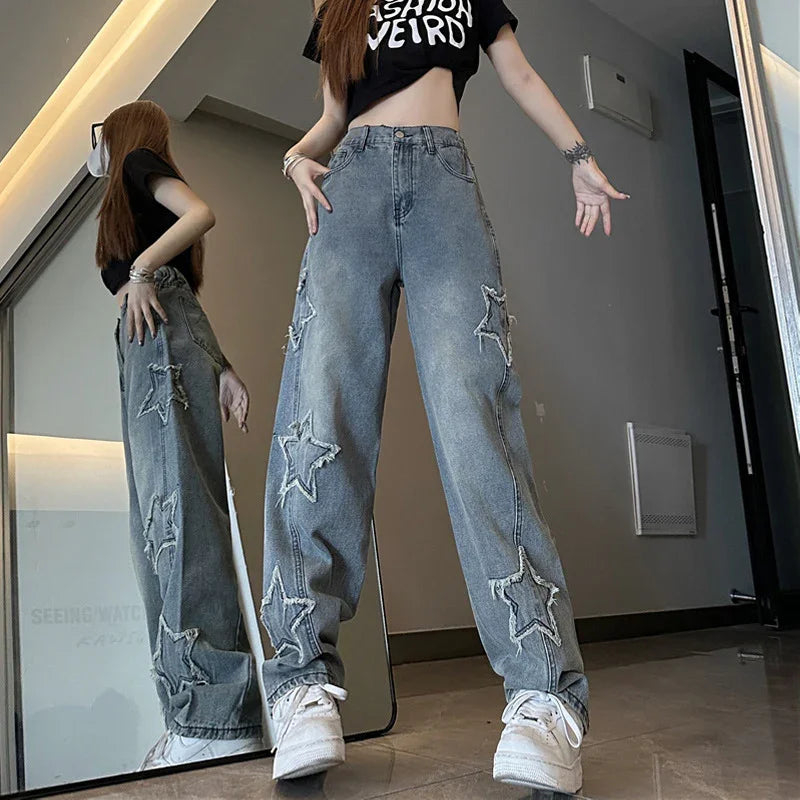 woman wearing high-waisted gray jeans with star patches and a black crop top reading Fashion Weird