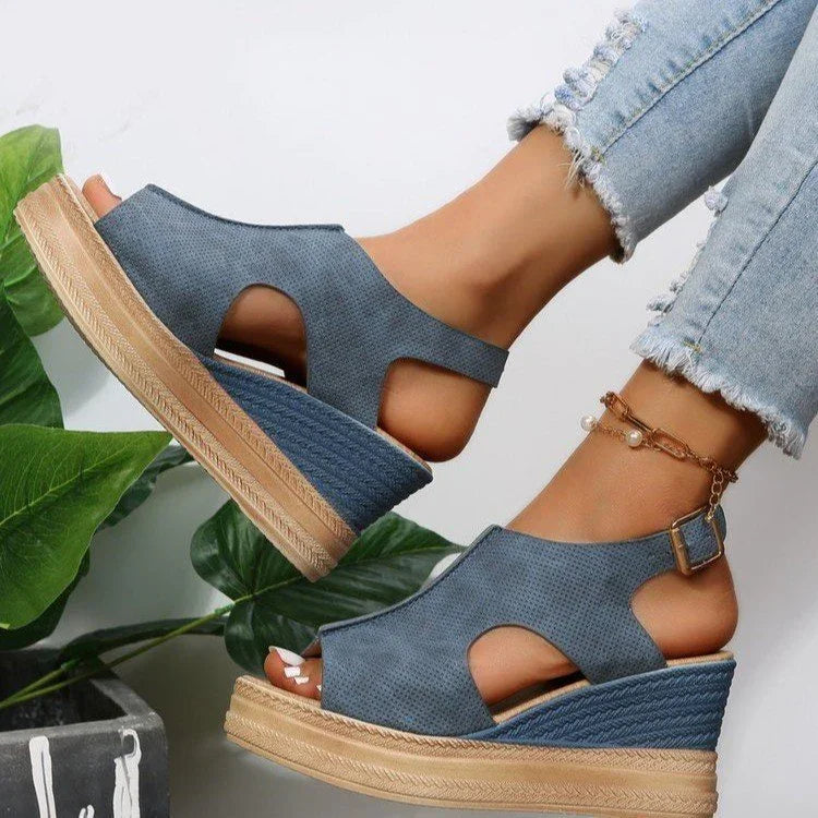 Blue wedge sandals with cutout design on feet, paired with light ripped jeans and anklet, green plant background