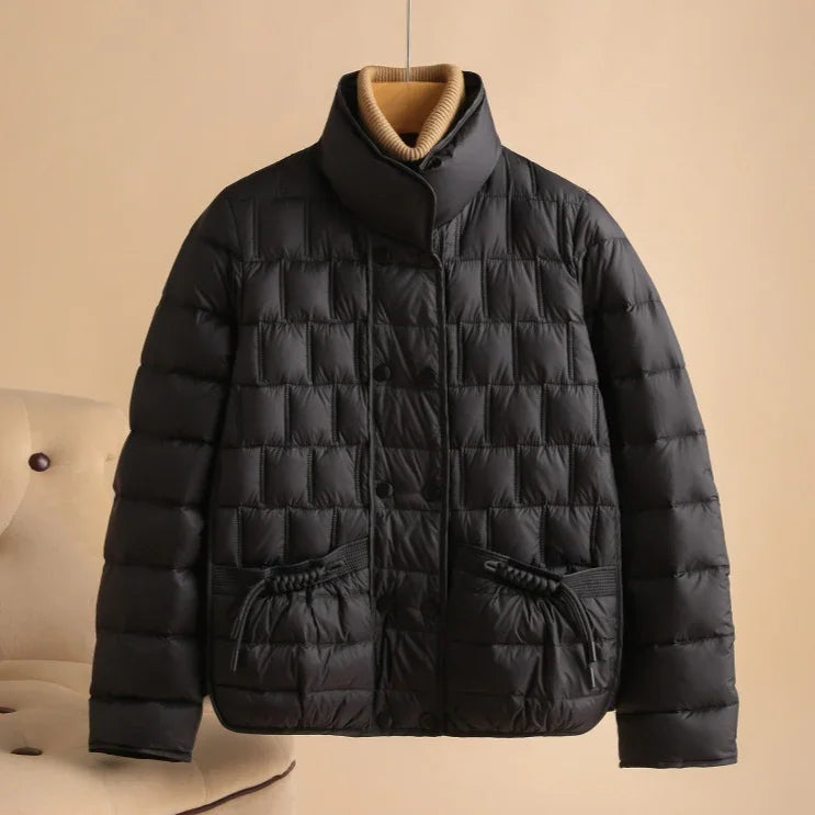 Black quilted puffer jacket with high collar and drawstring pockets on beige chair background