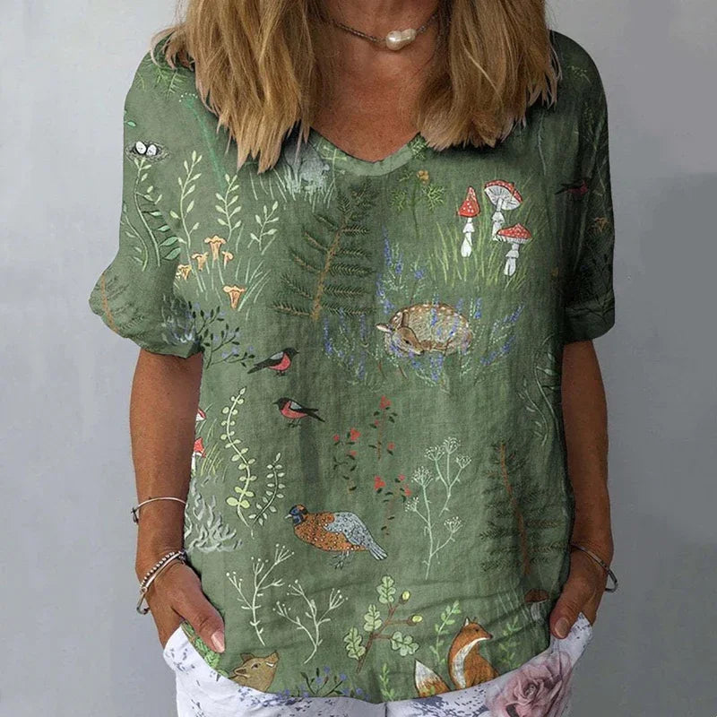 Woman wearing green nature-themed t-shirt featuring birds, fox, mushrooms, and plants, casual outfit