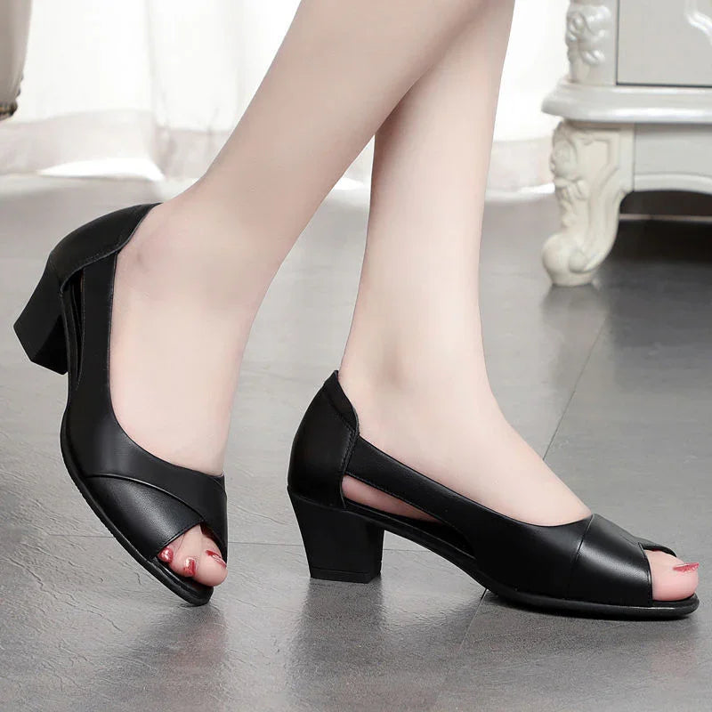 Black leather open-toe block heel shoes worn by model on gray floor indoors