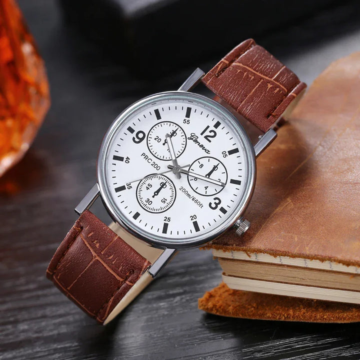 Geneva wristwatch with white dial, black numerals, and brown leather strap on a wooden table by a leather notebook