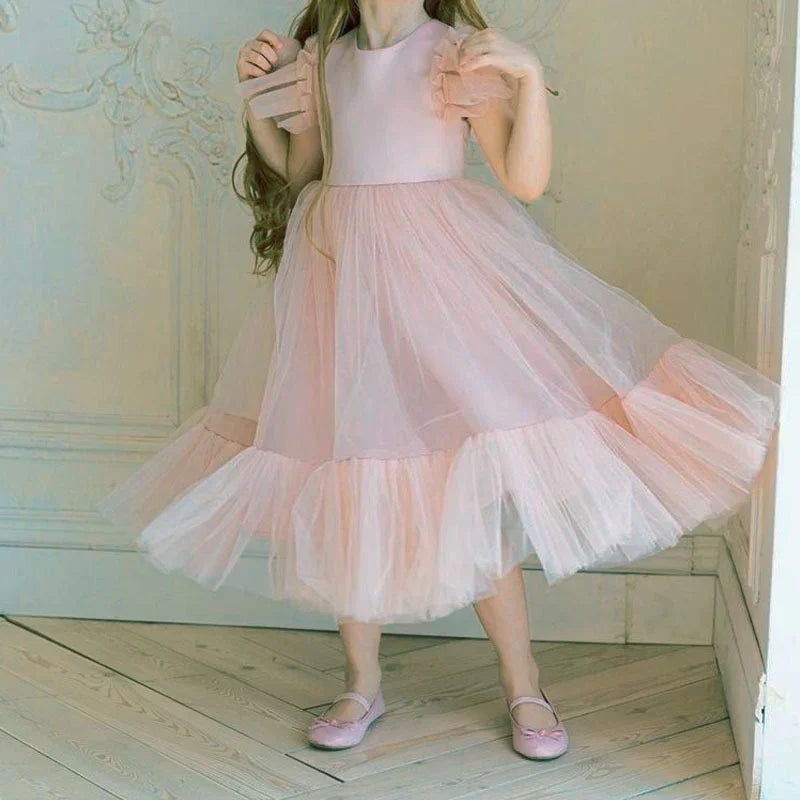 Little girl wearing a pink tulle dress and matching pink shoes standing on wooden floor indoors