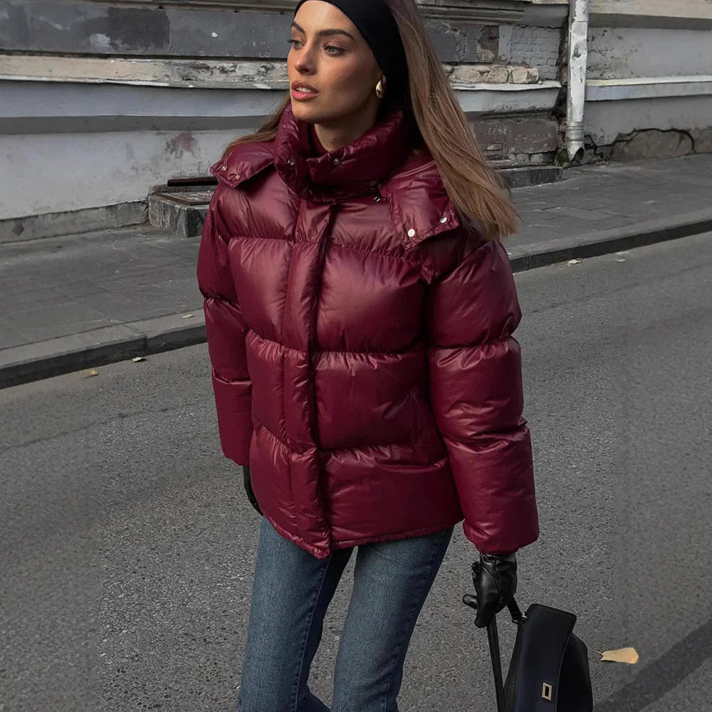 Woman in burgundy puffer jacket, blue jeans, black gloves, and headband walking on urban street