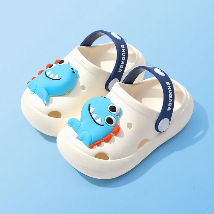 White toddler clogs with blue dinosaur cartoon decor and navy blue adjustable straps on light blue background