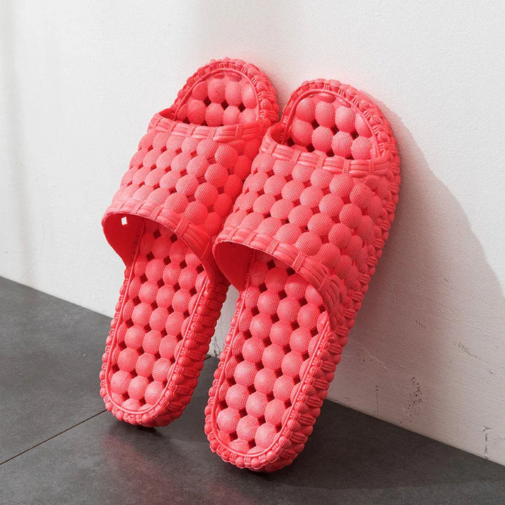 Pair of pink textured massage bubble sole slippers leaning against white wall on dark floor