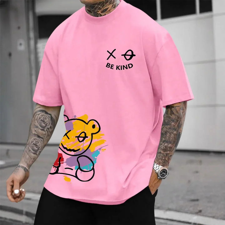 Man wearing pink t-shirt with colorful bear graphic and black text 'Be Kind' on chest