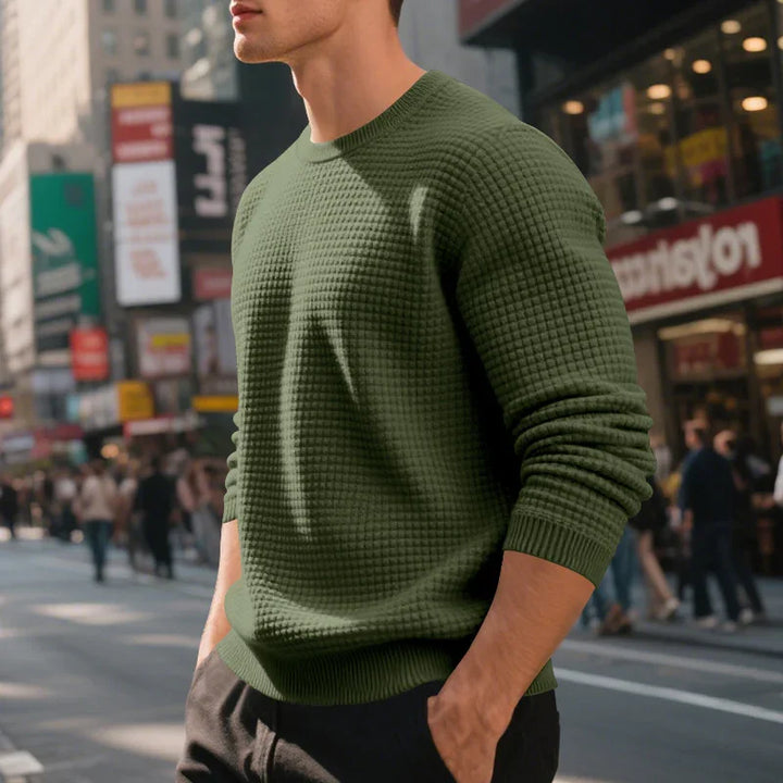 Man wearing textured olive green sweater with hands in pockets on busy city street