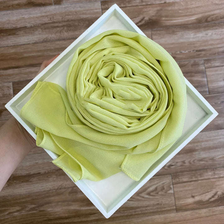 Hand holding white square tray with neatly rolled light green chiffon fabric on wooden floor