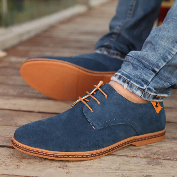 Blue suede casual shoes with brown sole and laces worn with rolled-up jeans on wooden floor
