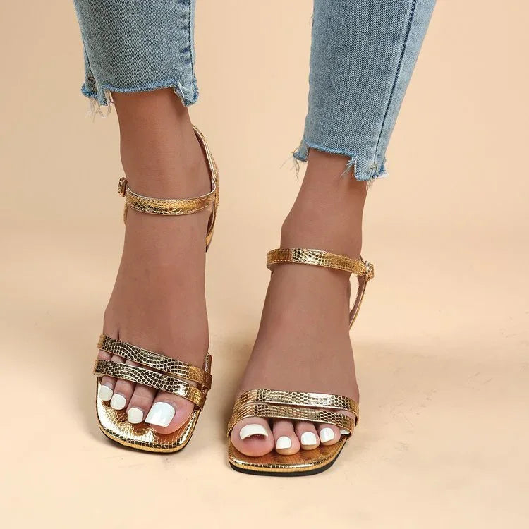 Woman wearing gold snake print ankle strap sandals with white pedicure and light blue frayed jeans