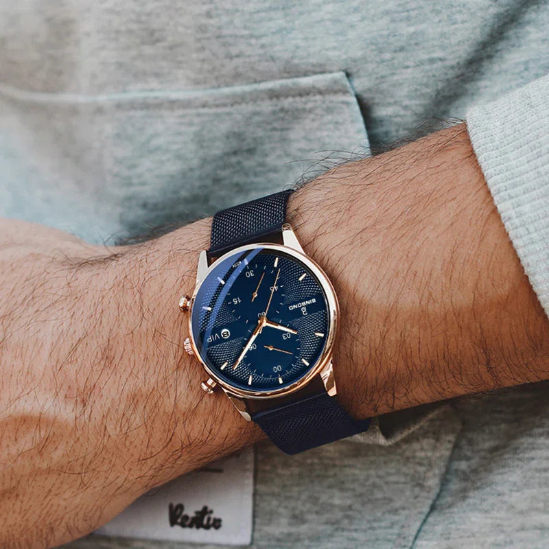 Close-up of a wrist wearing a blue and rose gold chronograph watch with a textured strap over a grey sweatshirt