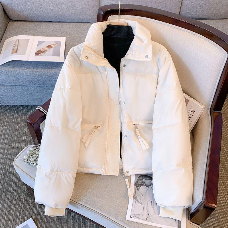 White puffer jacket with zipper and snap buttons on beige armchair, black turtleneck underneath