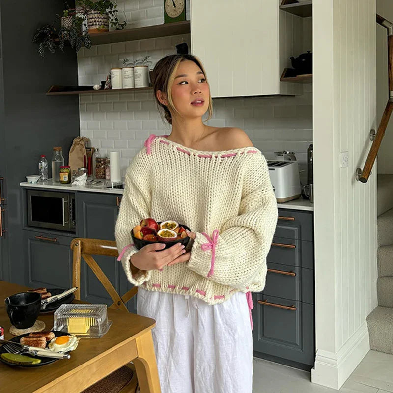 Young woman in cream knit sweater holding a bowl of fresh fruit in a modern kitchen with gray cabinets