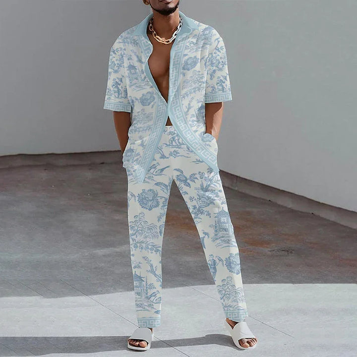Man wearing light blue and white floral patterned open shirt and matching pants with white sandals in minimalist setting