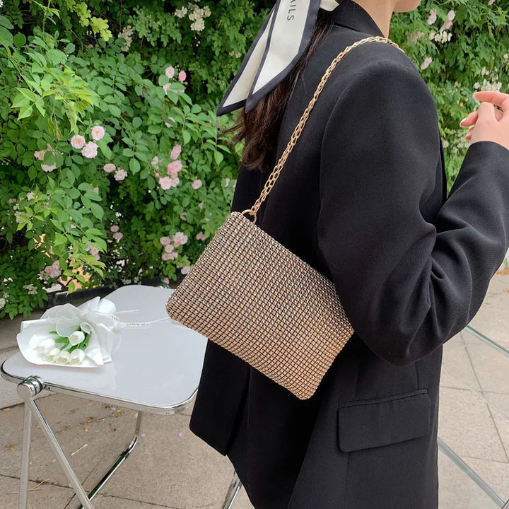 Woman in black blazer with checkered chain strap purse against green floral background and white table