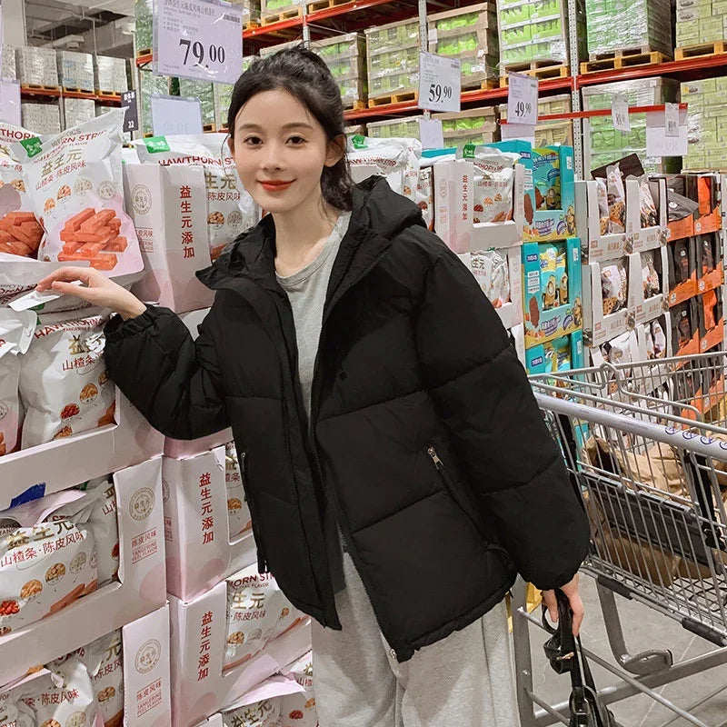 Young woman in black puffer jacket shopping in warehouse store aisle with packaged snacks and shopping cart