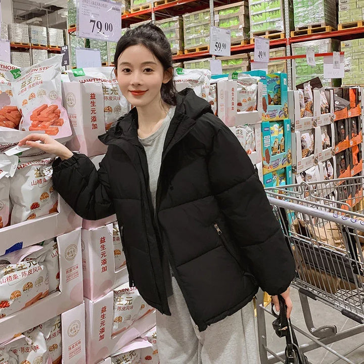 Young woman in black puffer jacket shopping in warehouse store aisle with packaged snacks and shopping cart