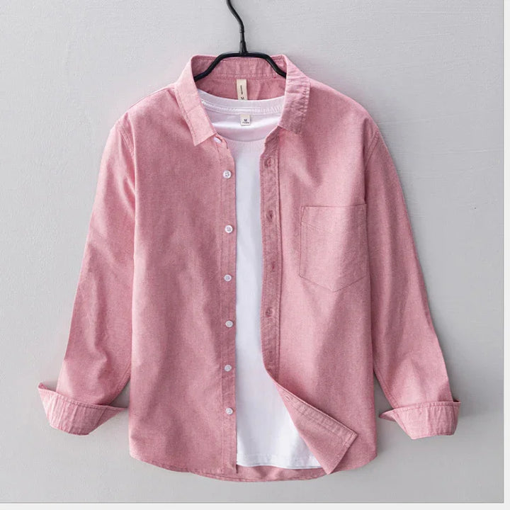 Pink button-up shirt with front pocket layered over white t-shirt on black hanger against gray background