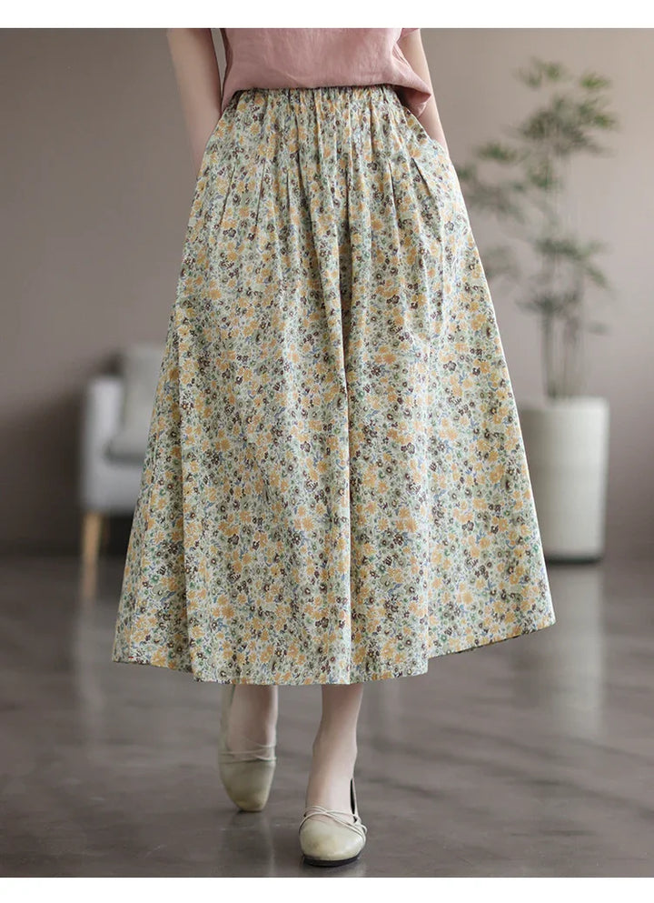 Woman wearing a long floral pleated skirt with pockets and beige flats in a modern indoor setting