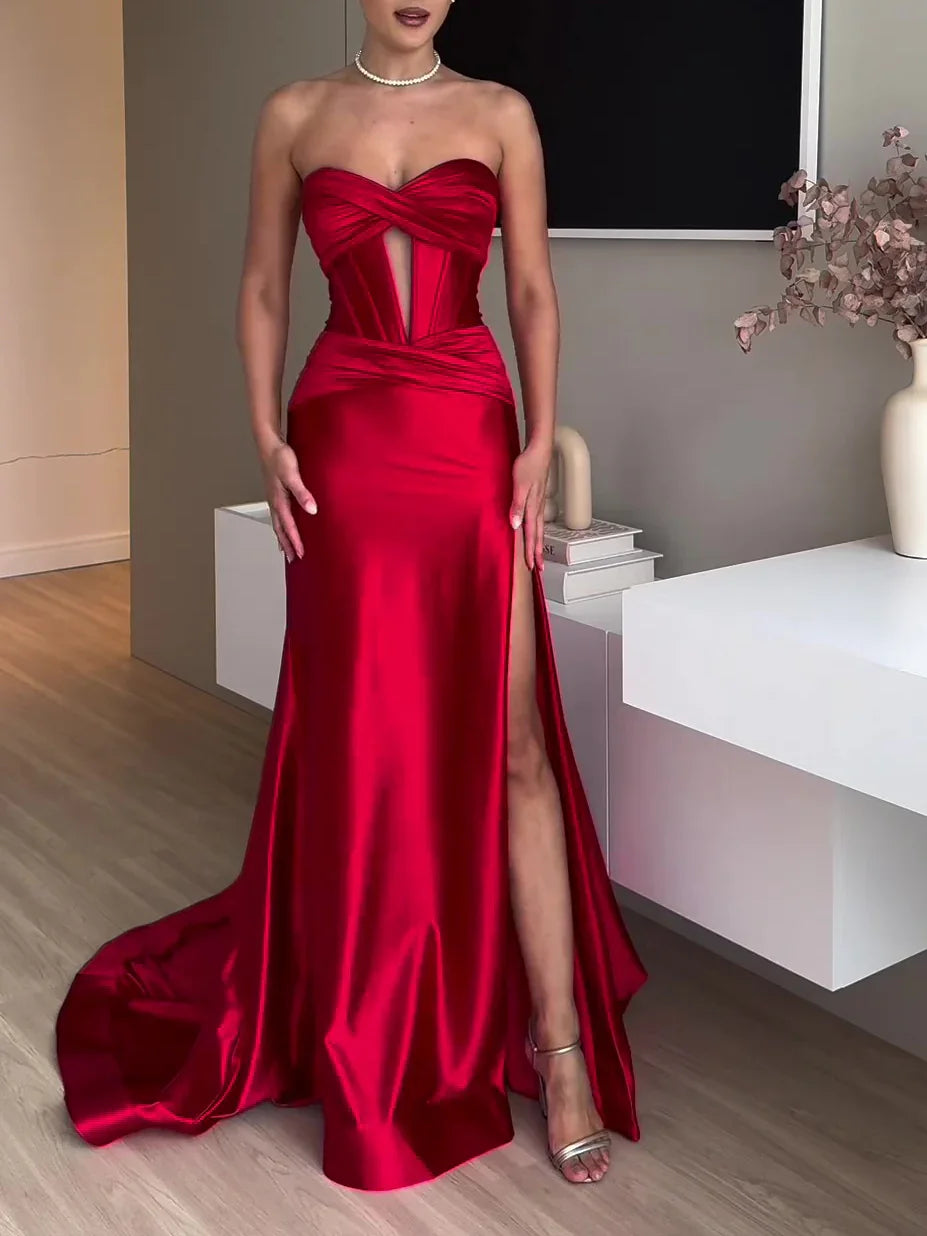 Woman wearing a strapless red satin evening gown with front slit and mesh cutout, standing indoors