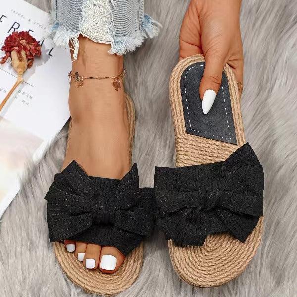 black bow slip-on sandals with rope soles worn on feet with white toenail polish and frayed jeans