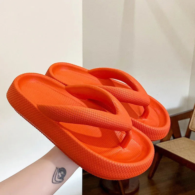 Hand holding bright orange textured foam flip flop sandals indoors