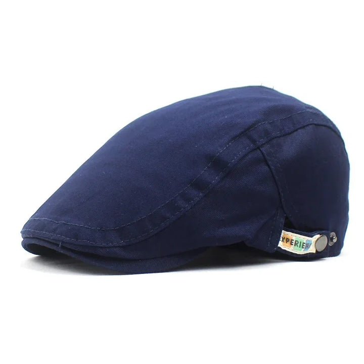 Navy blue flat cap with stitched seams and a small colorful fabric tag on the side