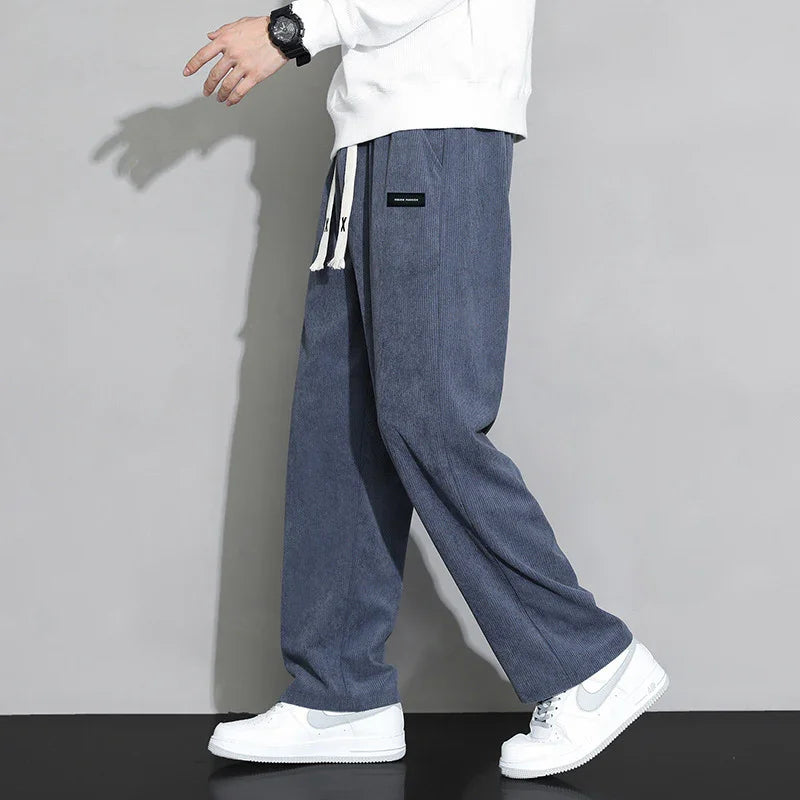 Man wearing blue wide-leg trousers with white drawstrings and white Nike sneakers against gray background