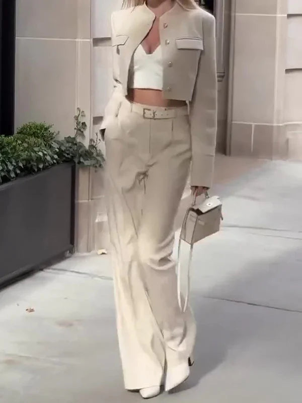 Woman wearing beige cropped blazer, high-waisted wide-leg pants, white crop top, and carrying a beige handbag on city sidewalk