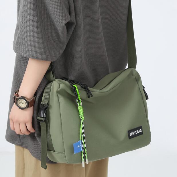 Person wearing gray top and beige pants carrying olive green SENYUBAG crossbody bag with neon cord zipper pulls