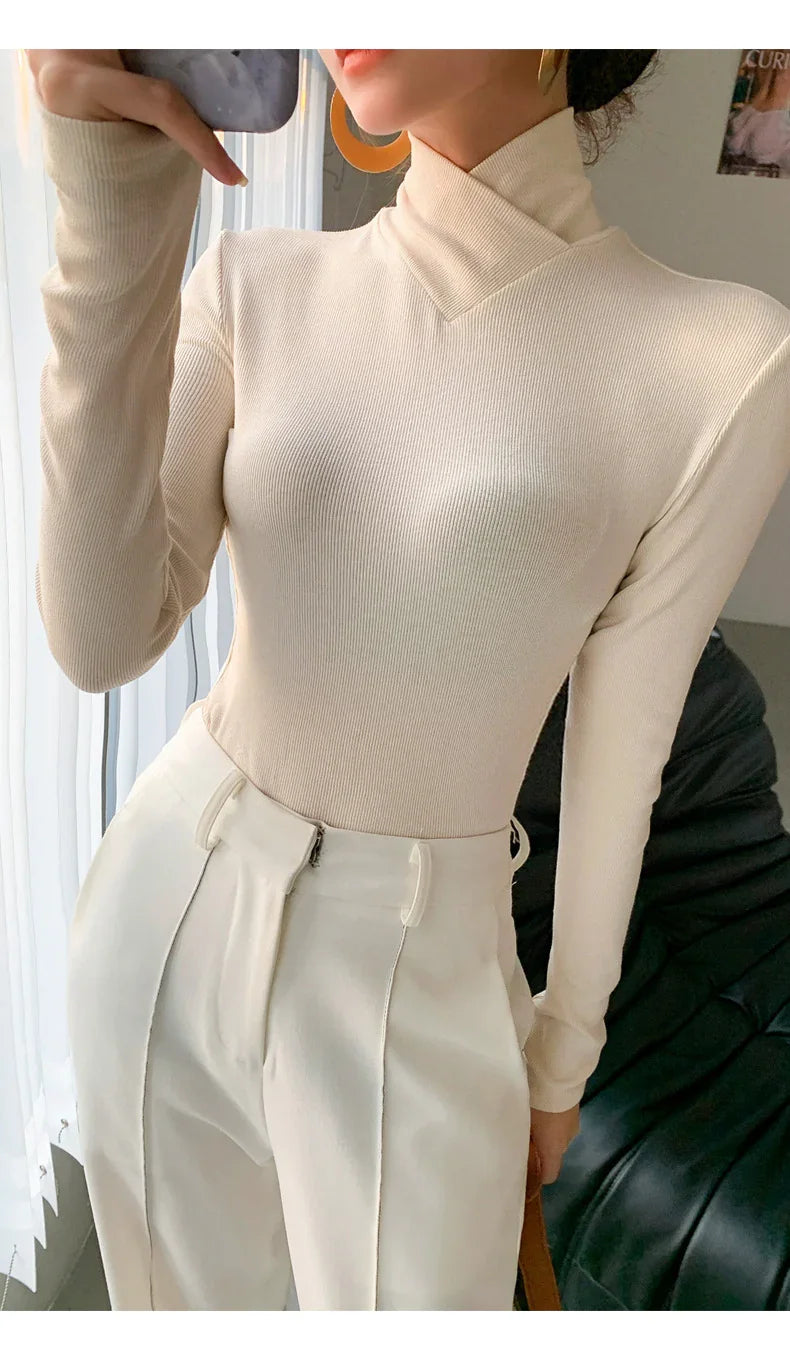 Woman wearing beige ribbed turtleneck sweater and high-waisted cream pants taking a mirror selfie