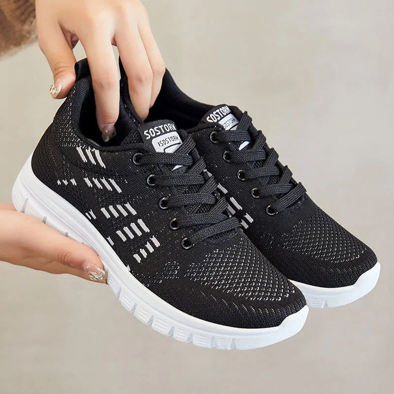Hand holding black lightweight knit sneakers with white sole and logo on tongue