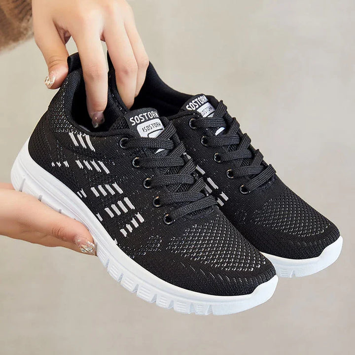 Hand holding black lightweight knit sneakers with white sole and logo on tongue