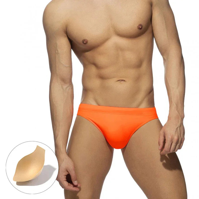 Muscular man wearing bright orange men's swim briefs with detachable padding insert shown