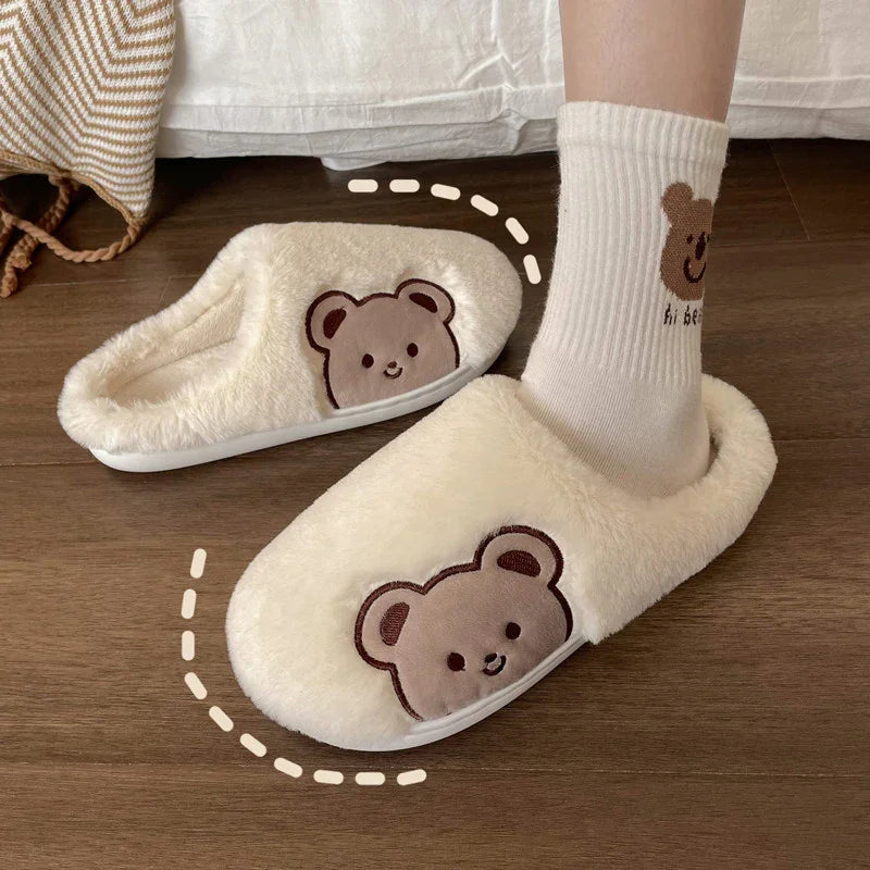 Cozy cream-colored fuzzy slippers with cute bear face embroidery on wooden floor