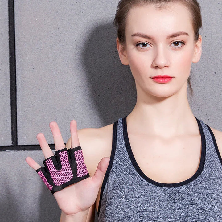 Young woman in gray sportswear showing pink and black fingerless workout gloves against a gray wall